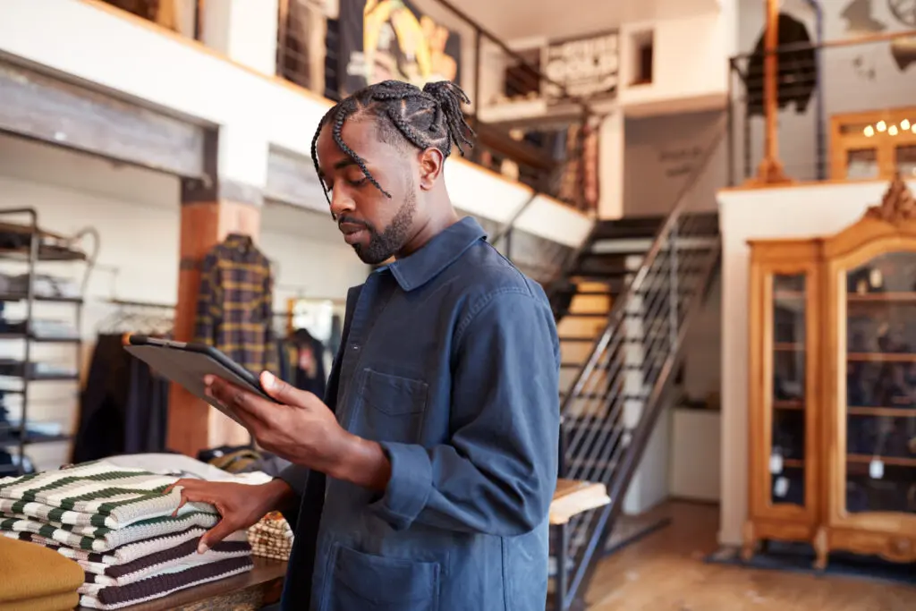 small business owner Of Fashion Store Using Digital Tablet To Check Stock In Clothing Store